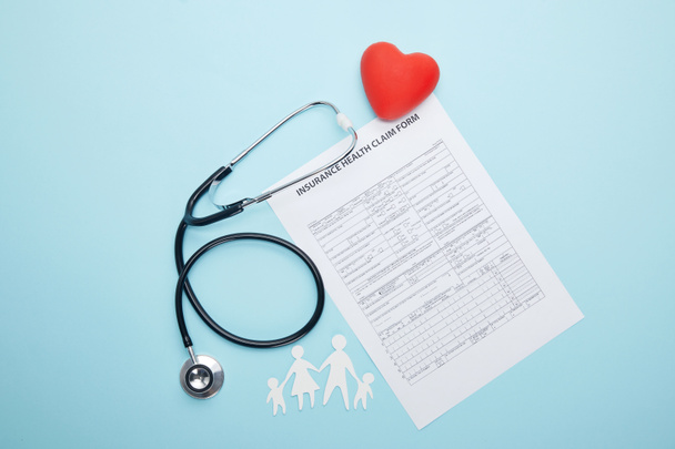 vue du dessus du stéthoscope, du formulaire de demande de règlement d'assurance maladie, du symbole du coeur rouge et de la famille coupée en papier isolée sur bleu
 - Photo, image