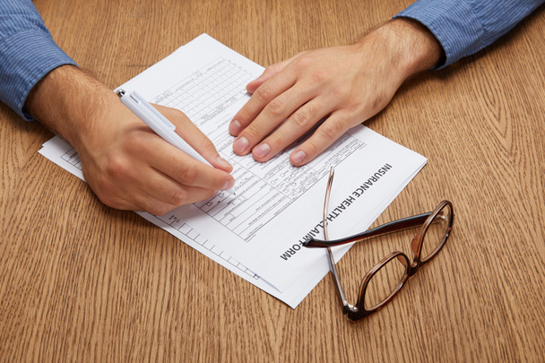 close-up partial view of person signing insurance form at wooden table   - Photo, image