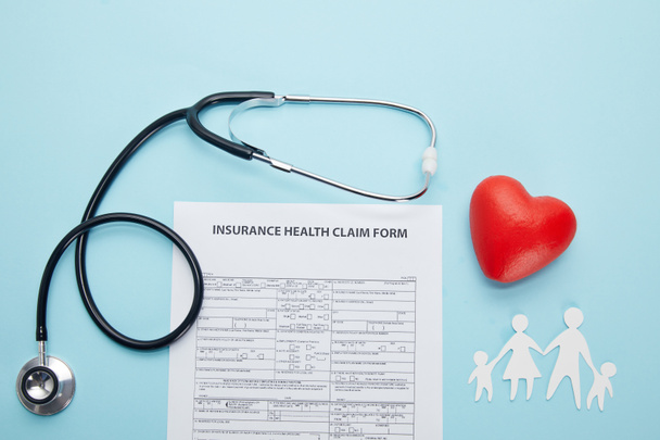 vue du dessus du formulaire de demande de règlement d'assurance maladie, de la famille coupée sur papier, du symbole du coeur rouge et du stéthoscope bleu
  - Photo, image