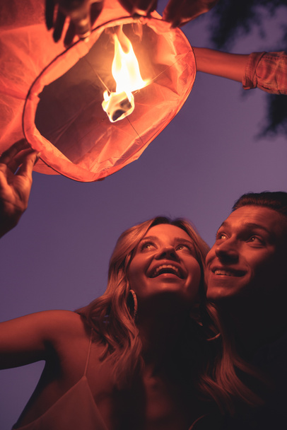 vista basso angolo di felice giovane coppia lancio lanterna cielo sulla spiaggia del fiume in serata
 - Foto, immagini