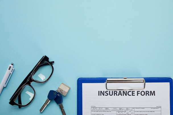 close-up view of insurance form, eyeglasses, pen and keys isolated on blue  - Photo, Image