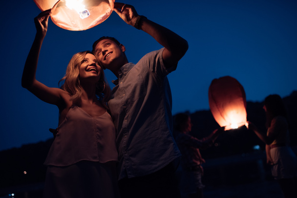 young couple launching sky lantern on river beach in evening - Photo, Image