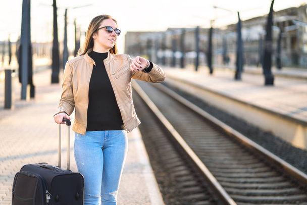 Ženy při pohledu na hodinky a čas při čekání na vlak. Usmívající se a šťastné ženské cestovatel stojící na nádraží a nástupiště. Negativní prostor pro kopírování. - Fotografie, Obrázek
