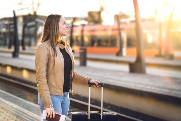 Smiling woman with luggage in train station. Happy lady standing with suitcase, passport and ticket at platform. Railway travel and lifestyle concept. - Fotoğraf, Görsel