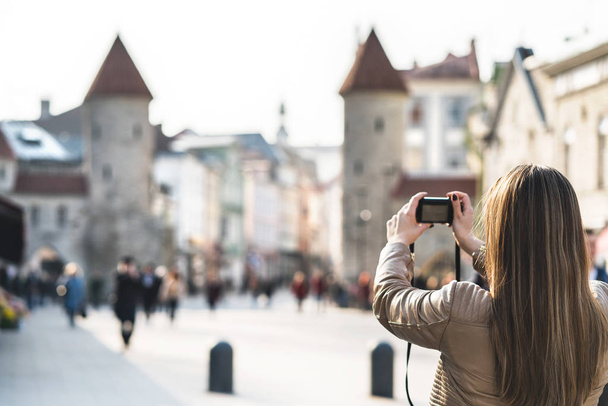 タリン ヴィル門の写真を撮影で観光。バカンス エストニアにおけるランドマークの写真を撮る女性。人気の街を歩いて人々。カメラを持つ少女の背面図. - 写真・画像