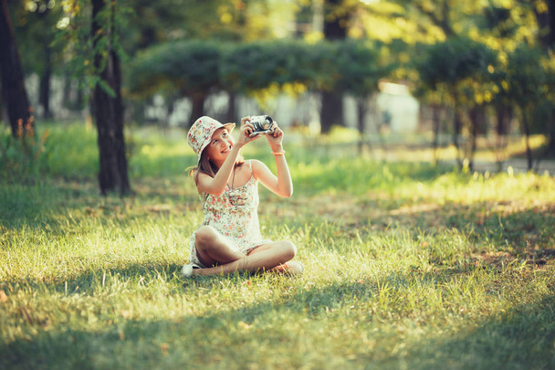 Das kleine Mädchen wird von einer Fotokamera gespielt, die auf Gras im Park sitzt. Selfie machen und die ganze Welt fotografieren - Foto, Bild