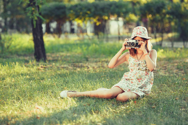 little girl is played by photo camera sitting on grass in park. Doing Selfie and photographing the world around - Photo, Image