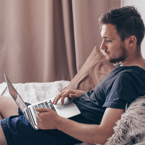 Πληκτρολογώντας νέο blog post. Τεχνολογία, home - lifestyle έννοια κοντινό πλάνο του ο άνθρωπος εργάζεται με φορητό υπολογιστή και να κάθεται στο κρεβάτι στο σπίτι - Φωτογραφία, εικόνα
