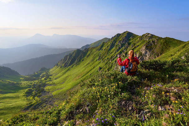 Серед диких гір квіти на краю скелі є дівчина, яка сидить і спостерігає за вершинами гір на горизонті. Скелясті гори
. - Фото, зображення