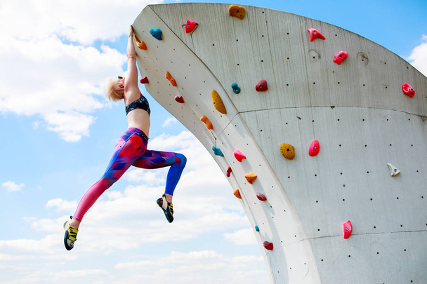 Photo of sporty girl in leggings hanging on wall for rock climbing against blue sky - Fotoğraf, Görsel