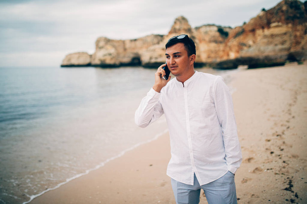 Giovane uomo sta usando il suo telefono sulla spiaggia al tramonto
 - Foto, immagini