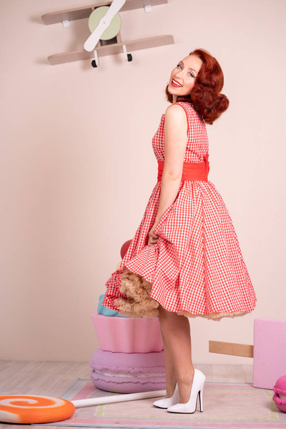 Beautiful red-haired pinup smiling happily girl posing in a retro red dress and white high heels - Foto, immagini