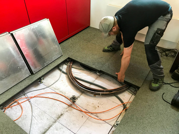 jonge mannelijke elektricien bezig met kabels in de ondervloer en het verwijderen van vloer panelen voor toegang - Foto, afbeelding