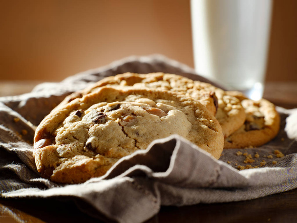 pile of chocolate chip cookies on napkin with tall glass of milk - Фото, зображення