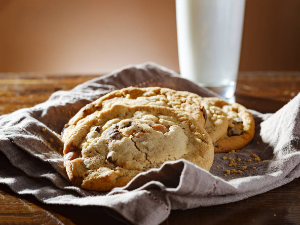 pile of chocolate chip cookies on napkin with tall glass of milk - Фото, зображення