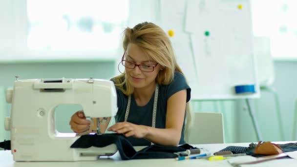Chica está cosiendo un paño en una máquina de coser, y sonriendo
. - Metraje, vídeo