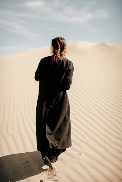 вид сзади женщины в черной абайе, идущей по пустыне
 - Фото, изображение