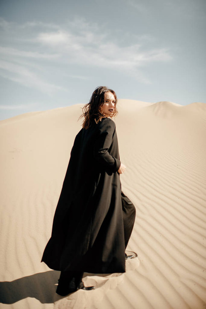 Achteraanzicht van de vrouw in zwarte abaya lopen in de woestijn - Foto, afbeelding