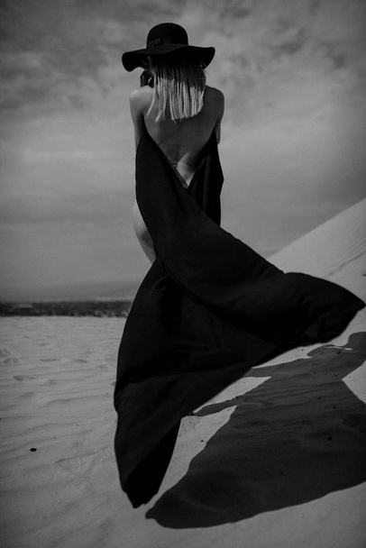Mooi meisje in een zwarte jurk op de woestijn - Foto, afbeelding