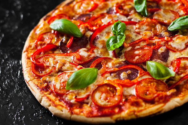 Pizza con queso Mozzarella, Jamón, Tomates, salami, pimienta, pepperoni Especias y Albahaca Fresca. Pizza.on italiano fondo negro
 - Foto, Imagen