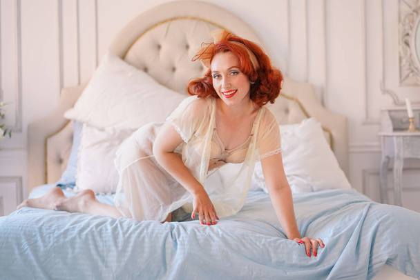 Een luxe pin-up dame gekleed in een beige vintage lingerie poseren in haar slaapkamer alleen - Foto, afbeelding