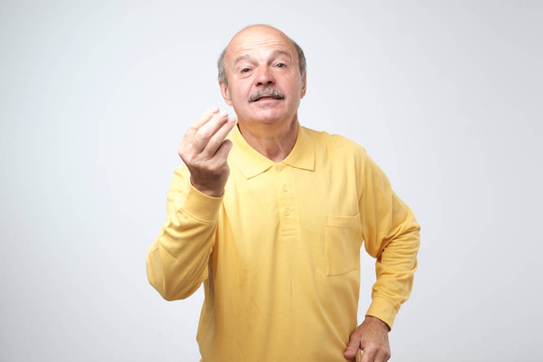 Portrait of mature handsome man in yellow shirt showing italian gesture that means what do you want over white background. Bald gloomy guy do not have clue of what happening - Photo, Image