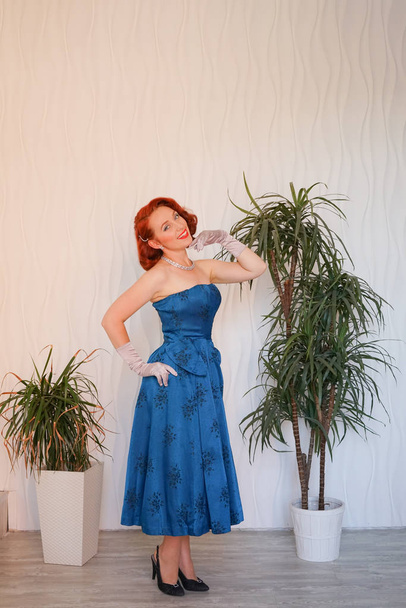 Mujer vintage hermosa educada vestida con vestido retro azul de pie solo en la habitación blanca vacía
 - Foto, Imagen