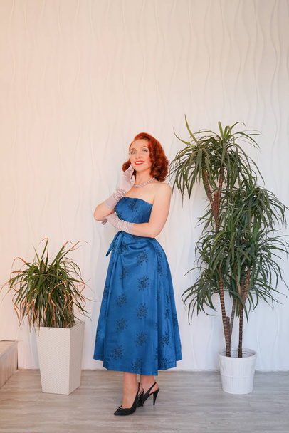 Mannered beautiful vintage woman dressed in blue retro dress standing alone in the empty white room - Foto, Imagen