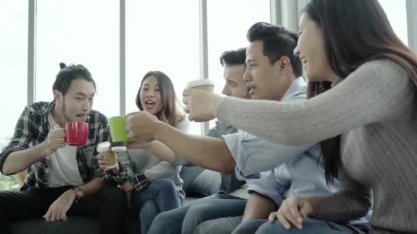 Diversidad de los jóvenes equipo de grupo sosteniendo tazas de café y discutir algo con sonrisa mientras se sienta en el sofá en la oficina. Tiempo de descanso de café en la oficina creativa
. - Imágenes, Vídeo