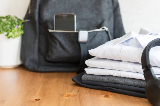 Back to school concept, backpack with school uniform such as white shirts and sweater, as well as electronic devices such as smart watch, mobile phone and headphones on the light background - Photo, Image