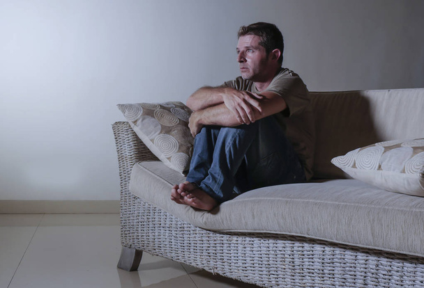 lifestyle dramatic light portrait of young sad and depressed man sitting at shady home couch in pain and depression feeling stressed and desperate crying alone suffering anxiety crisis - Foto, Imagen