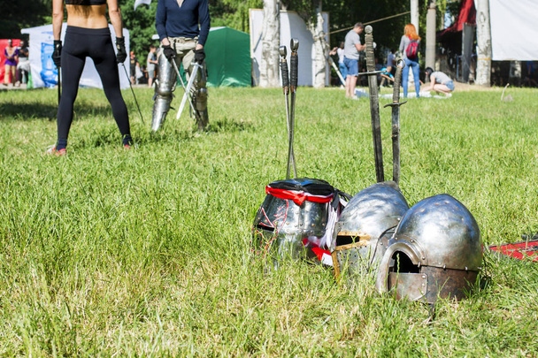 Лицарські каски лежать на траві на тлі боїв з мечами
 - Фото, зображення