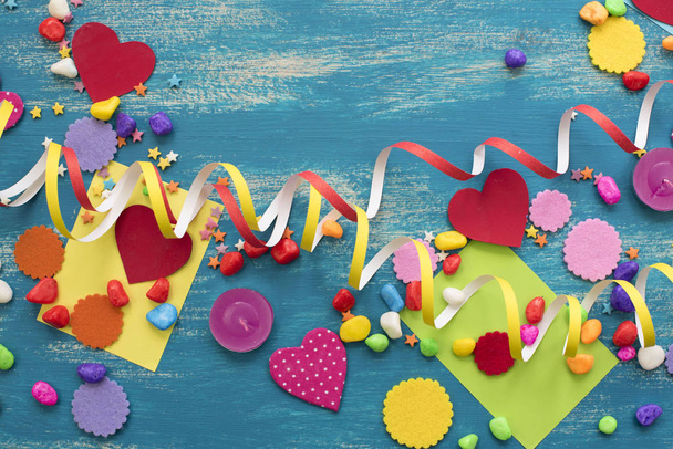 Decoratieve vakantie achtergrond met streamers confetti snoep harten decor. Blauwe armoedige houten bovenaanzicht achtergrond plat leggen - Foto, afbeelding