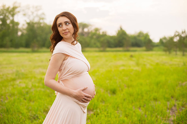 Felice donna incinta che cammina nel campo verde nel parco all'alba con una calda luce posteriore sullo sfondo
 - Foto, immagini