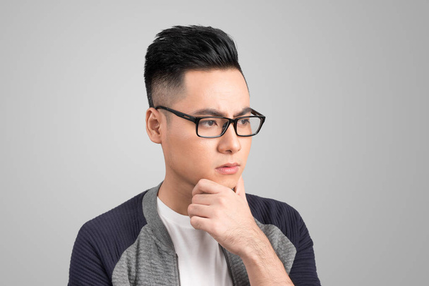 ritratto di un giovane uomo asiatico pensando guardando verso il basso isolato su sfondo grigio
 - Foto, immagini