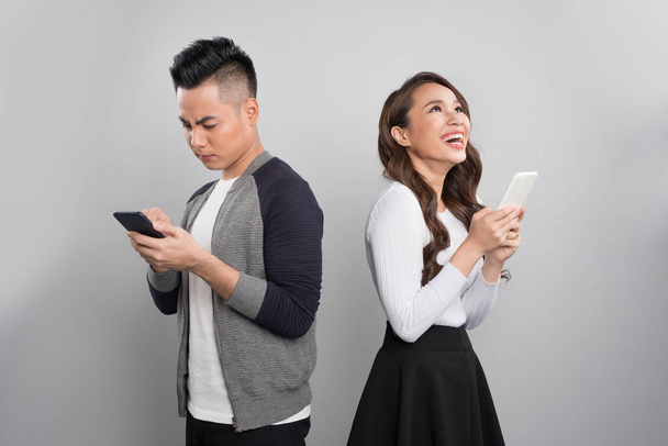 Молодая пара стоя спиной друг к другу и глядя на телефон, в то время как мужчина грустно и женщина взволнована
. - Фото, изображение