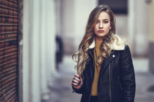 Blondine mit urbanem Hintergrund. schönes junges Mädchen in schwarzer Lederjacke und Minirock, das auf der Straße steht. hübsche russische Hündin mit langen welligen Haaren und blauen Augen. - Foto, Bild