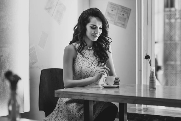 Jovem mulher sentada no interior do moderno café urbano movendo colher de chá em xícara de café. Fresco jovem modelo feminino caucasiano moderno em seus 20 anos
. - Foto, Imagem
