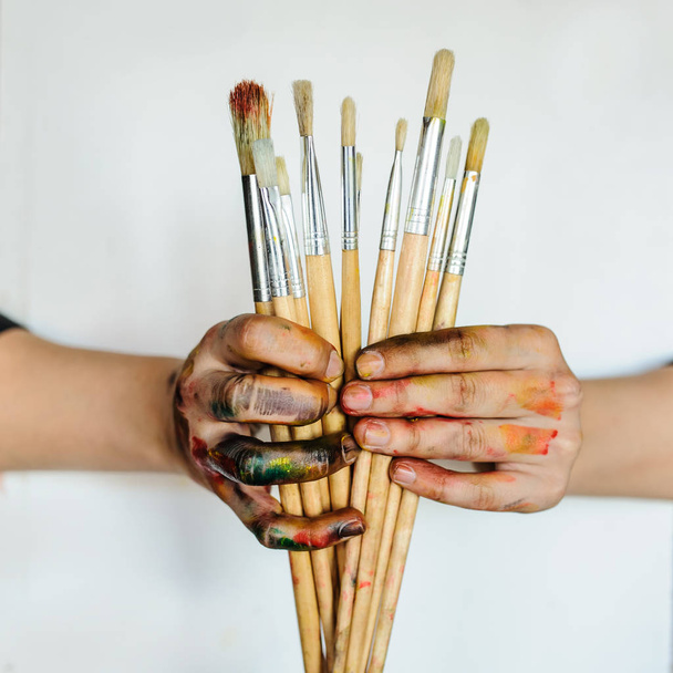 Close Up de um artista / pintor mãos segurando pincéis de pintura. Sujo pintado com tinta colorida sobre fundo branco
 - Foto, Imagem