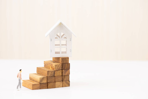Miniatur-Menschen kleine Figur zu Fuß zum Modell weißen Hauses auf Holzblock stapeln Treppe. Immobilieninvestitionen und Haus Hypothek Finanzkonzept, Eigenheimschutz, Versicherung. mit Kopierraum. - Foto, Bild