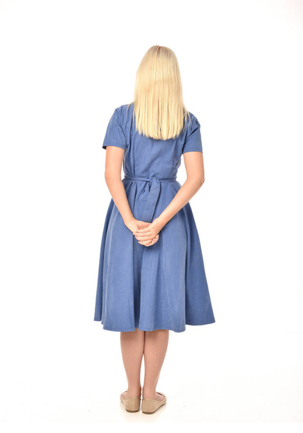 Ολόσωμο πορτρέτο του ξανθιά κοπέλα φορώντας μπλε φόρεμα. στέκεται ποζάρουν με πλάτη στην κάμερα. απομονωμένα σε φόντο λευκό στούντιο. - Φωτογραφία, εικόνα