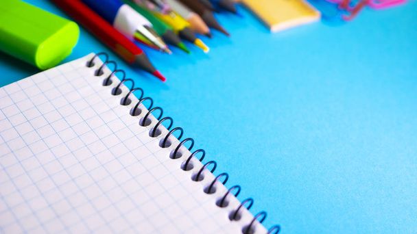 Schulbedarf auf blauem Hintergrund. Stifte, Bleistifte, Lineal, Büroklammern, Notizbuch für Copyspace und Marker auf dem Tisch. Blick von oben mit Kopierraum - Foto, Bild