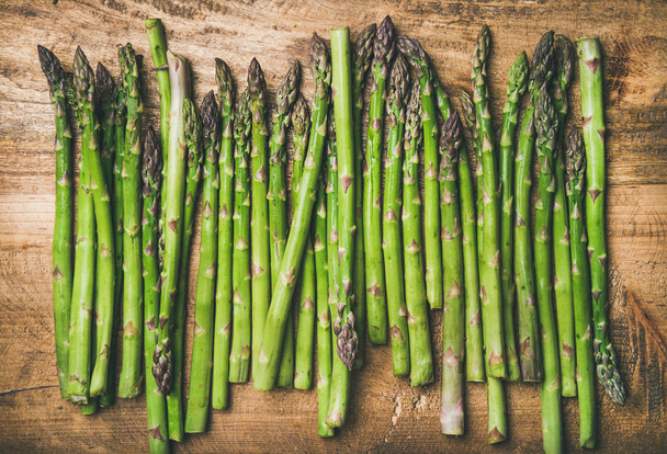 raw uncooked green asparagus in row over rustic wooden background - Foto, afbeelding