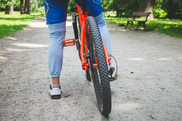 Pernas de um ciclista e parte de uma bicicleta em uma estrada de terra
. - Foto, Imagem