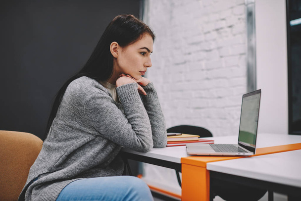 Young pretty concentrated female student dressed in stylish outfit carefully watching training webinar in website on laptop, skilled hipster girl analyzing information from network during work - Fotó, kép