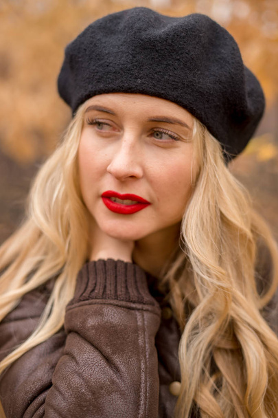 girl blonde in a black beret with bright red lips against the backdrop of an autumn garden - 写真・画像