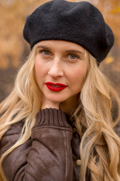 girl blonde in a black beret with bright red lips against the backdrop of an autumn garden - Foto, Bild