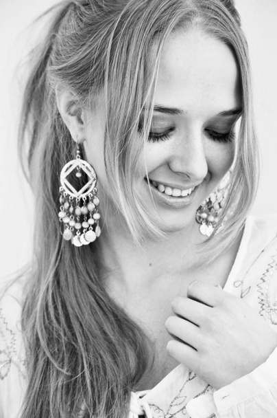 smiling young woman with long blond hair and arabian style earrings. Black and white. - Photo, Image