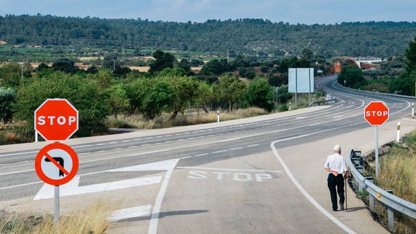 Älterer Mann läuft mit dem Stock an einem roten Stoppschild vorbei, das zu einer kurvenreichen Autobahn führt - konzeptionelles Bild - Foto, Bild