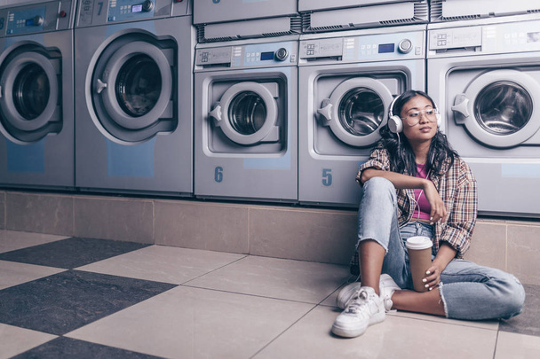 Chica que espera con auriculares en la lavandería
 - Foto, Imagen